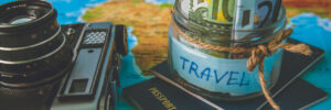 Vacation budget concept. Vacation money savings in a glass jar on world map with retro camera and passport