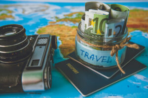 Vacation budget concept. Vacation money savings in a glass jar on world map with retro camera and passport